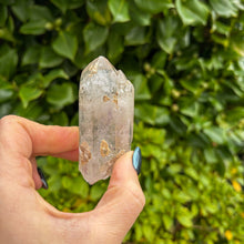 Load image into Gallery viewer, Hand holding a crystal against a green leafy background
